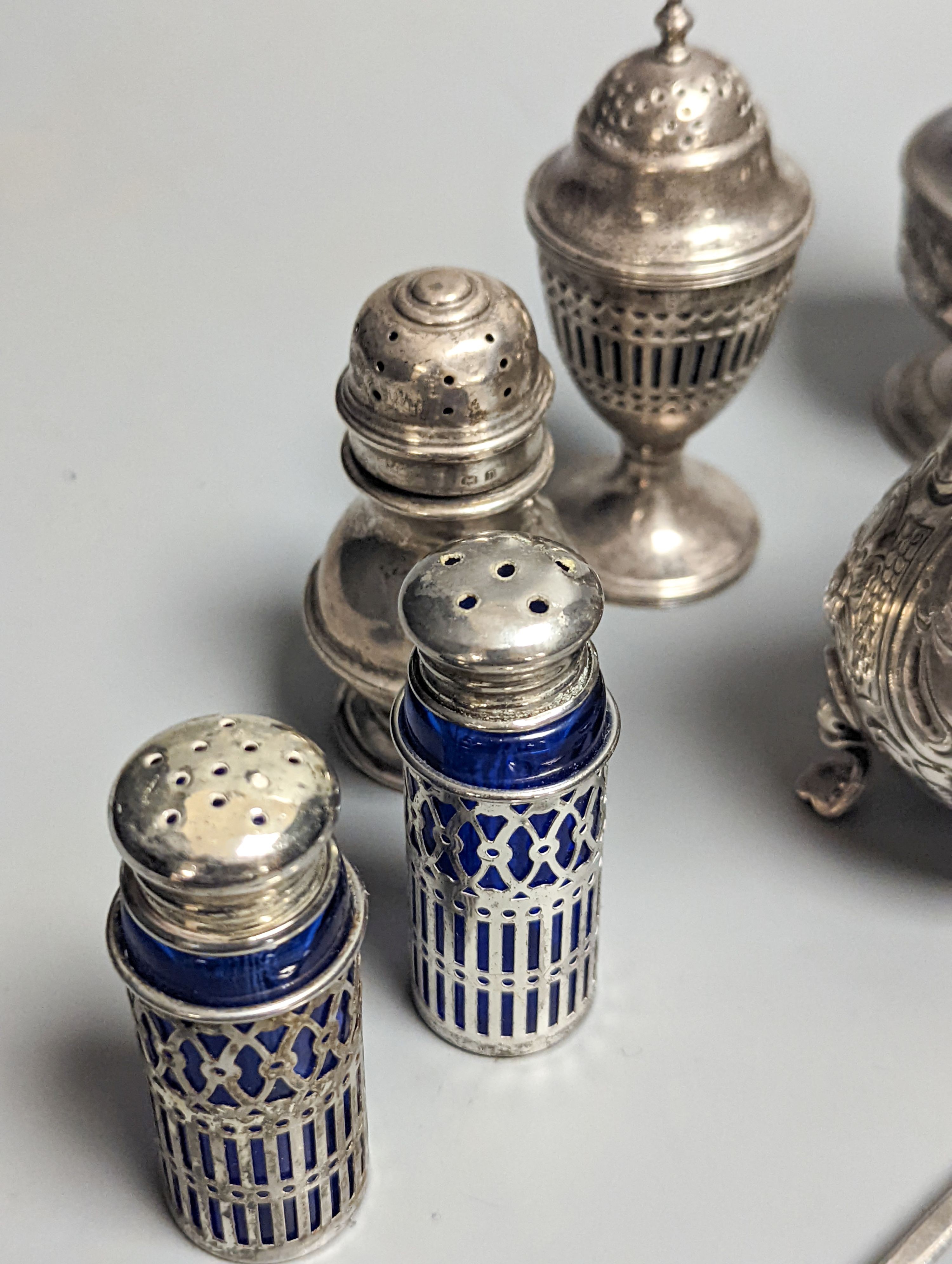 A Victorian embossed silver cream jug, London, 1883, 92mm, two 18th century silver pepperettes, one with plated cover, four later condiments (two silver), a silver spoon and small 800 standard photograph frame.